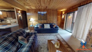 Un intérieur de chalet chaleureux avec un canapé bleu, un divan à carreaux, des murs en bois et un coin cuisine.