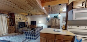 Cozy living room with a fireplace, TV, and comfortable sofa, featuring a kitchen area with a stove and dining table.