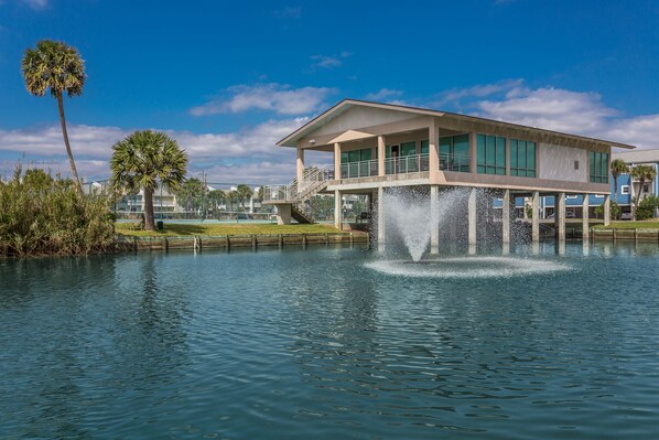 A waterfront property with a modern house, a fountain, and a dock extending into a calm lake.