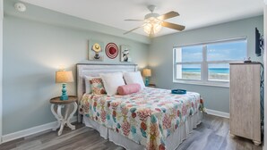 Un dormitorio con cama, ventilador de techo, ventana con vistas y mesita de noche con lámpara.