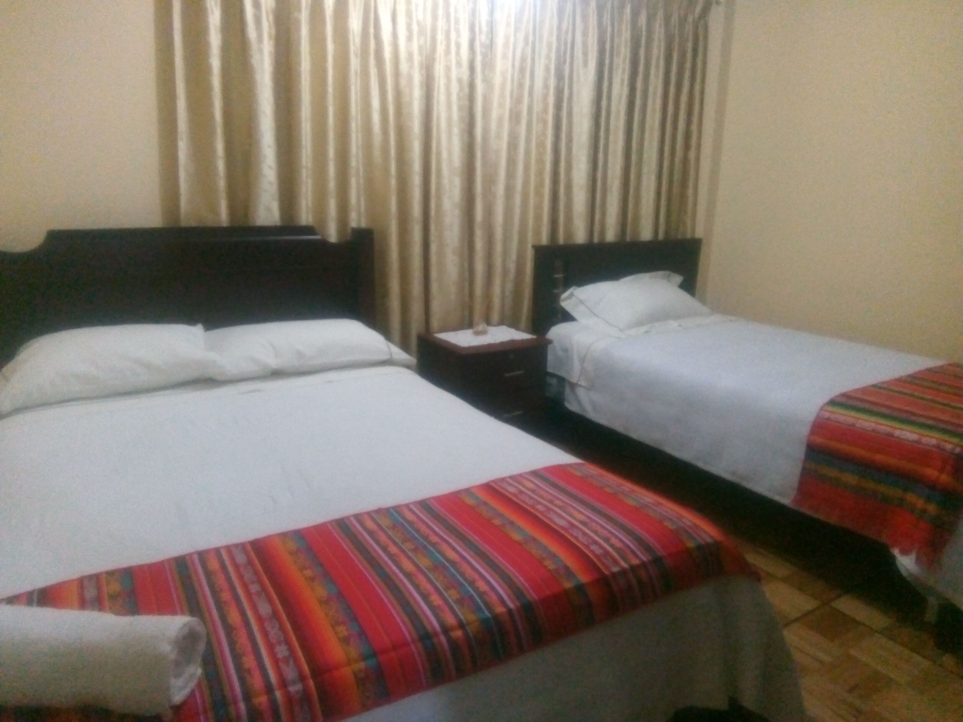 A hotel room with two single beds, a nightstand, and a curtain.