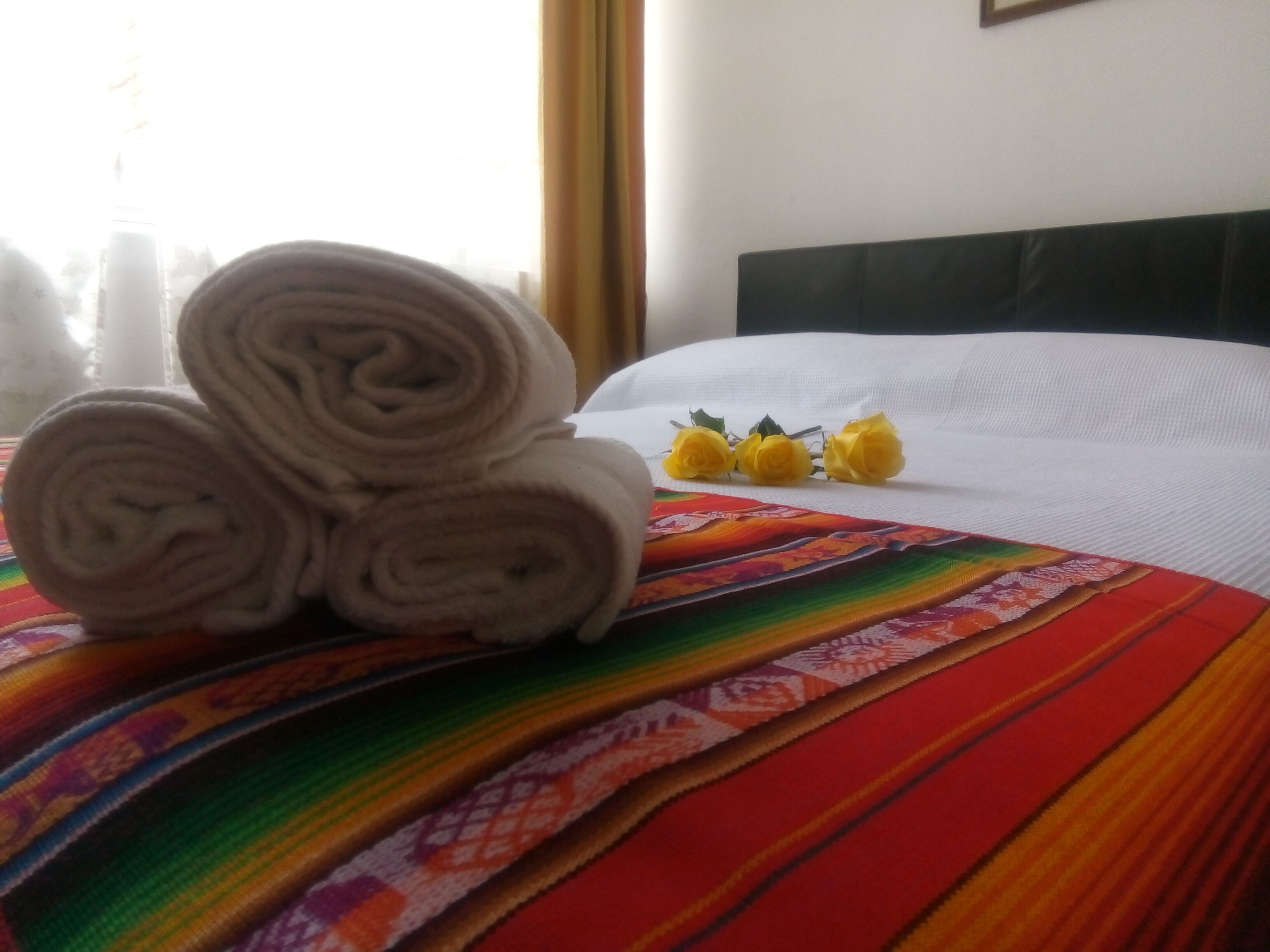 Een bed met gerolde handdoeken en gele bloemen op een kleurrijke deken.