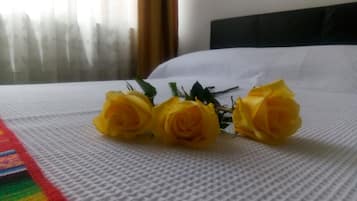 Una cama con una colcha blanca con textura y un ramo de rosas amarillas sobre ella.