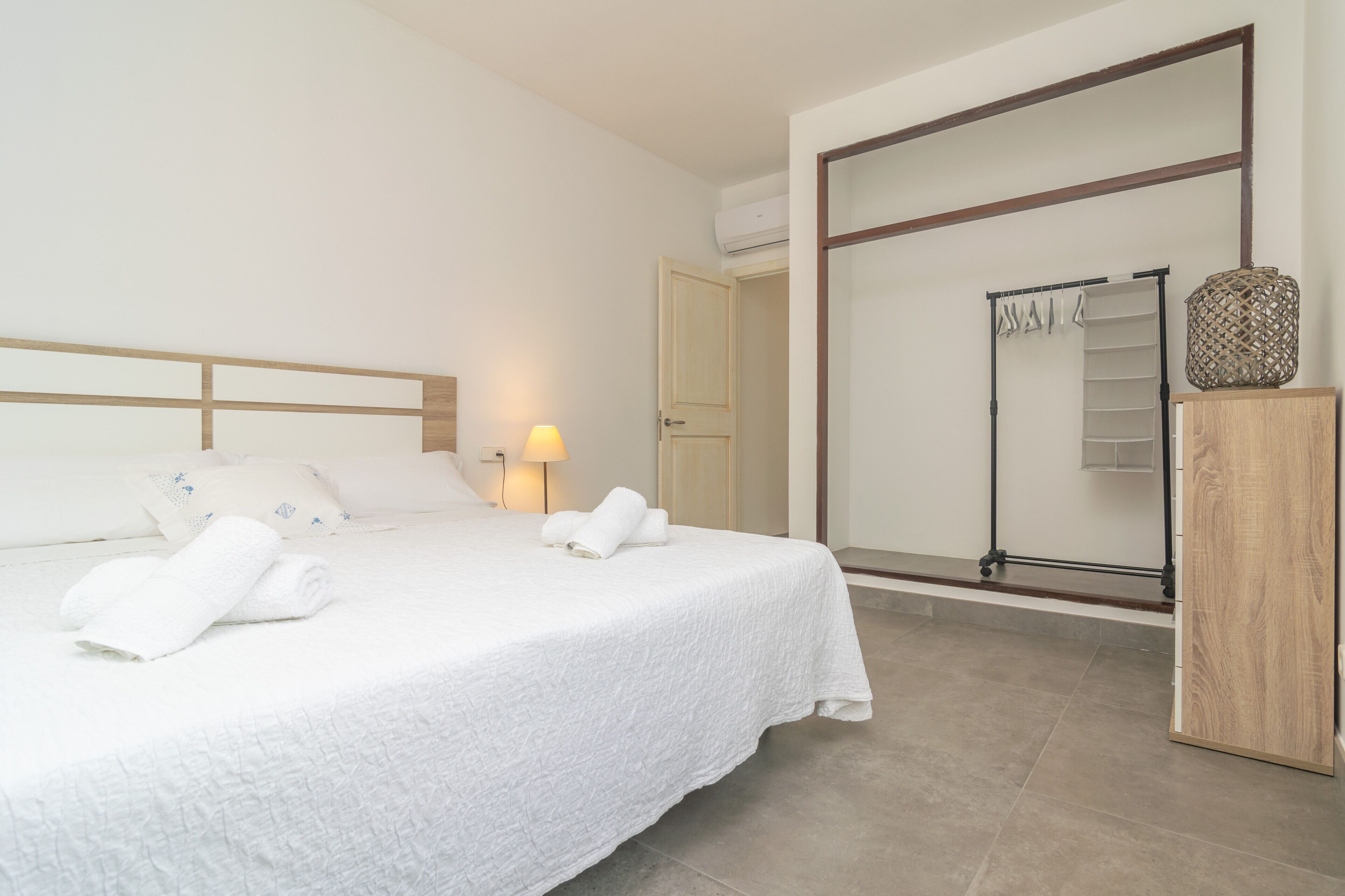 A neatly made bed with white linens and towels, a wooden headboard, a bedside lamp, and a wooden cabinet.