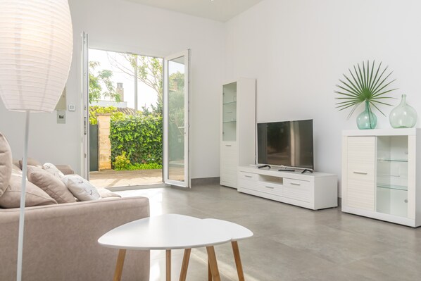 A modern living room with a sofa, a white coffee table, a flat-screen TV, and a glass cabinet.