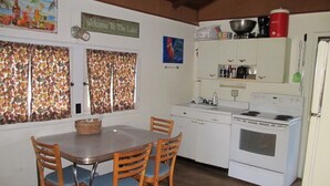 A compact kitchen with a stove, sink, and cabinets. There is a dining table with chairs and a window with curtains.