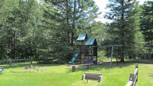 A playground with a slide and climbing area, surrounded by trees.