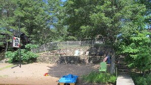 A wooden dock leading to a small boat on a muddy shore with a stone wall and a wooden fence in the background.