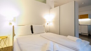 A hotel room with a neatly made bed, two wall-mounted lamps, and a visible bathroom in the background.