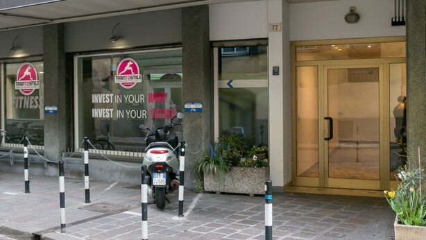 A modern building entrance with a sign reading "TRIANTOSMILE FITNESS INVEST IN YOUR FITNESS."