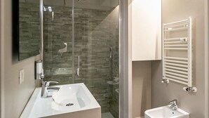 A modern bathroom with a glass shower enclosure, a large mirror, and a white sink with a bidet.