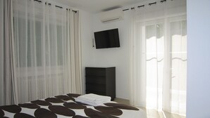 Una camera da letto con un letto, una televisione a parete e un'ampia finestra con tende leggere.