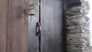 A wooden door with a metal handle and a bell, set in a rustic building with a stone wall and wooden beams. - Chalet / stone house (Sainte-Foy-Tarentaise)