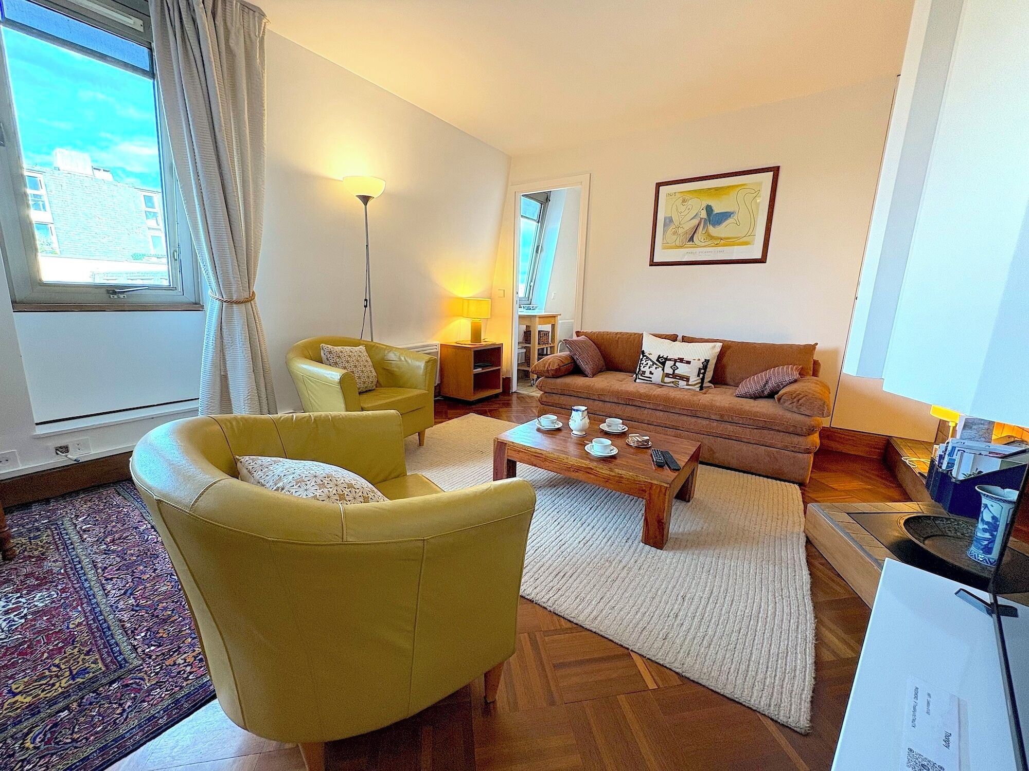 Una sala de estar con un sillón amarillo, un sofá marrón, una mesa de centro y una lámpara.