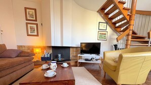 A living room with a sofa, yellow armchair, coffee table, fireplace, TV, and a wooden staircase. - Le Penthouse Thorigny (Paris)