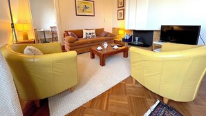 A living room with yellow sofas, a wooden coffee table, a TV, and a fireplace. - Le Penthouse Thorigny (Paris)