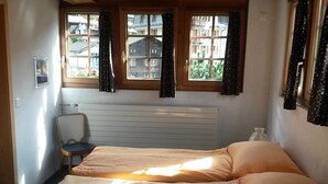 A bedroom with two beds, a radiator, a chair, and a window with curtains. - ABC Ferienwohnung 1 1. OG Süd by Interhome (Fiesch)