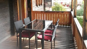 A wooden deck with a table and chairs, overlooking a street with buildings. - ABC Ferienwohnung 1 1. OG Süd by Interhome (Fiesch)
