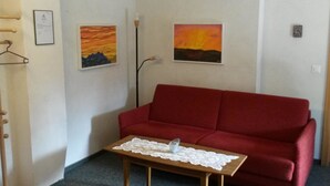 A red sofa, a small wooden table with a lace tablecloth, and two paintings on the wall. - ABC Ferienwohnung 1 1. OG Süd by Interhome (Fiesch)