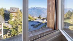 A mountain view from a window with wooden beams, a view of a parking area, and a building with a sloped roof.