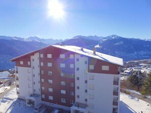 A multi-story hotel with a red and white facade, located in a snowy mountainous area with a clear view of the surrounding peaks. - Belmont Est 80 by Interhome (Crans-Montana)