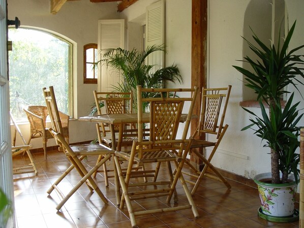A room with a wooden table and chairs, a potted plant, and a view of the outdoors.