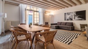 Un salon moderne avec une table à manger en bois, des chaises en osier, un canapé gris et un tapis noir et blanc.