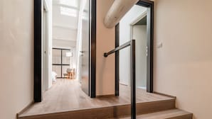 Un escalier avec des marches en bois et une rampe en métal, menant à une pièce dotée d’une grande fenêtre et offrant une vue sur une autre pièce.