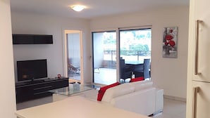 A modern kitchen with white cabinetry, a large island, and a dining area with a white sofa and red cushions.