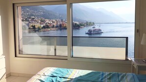 A hotel room with a large window offering a view of a lake, boats, and a mountainous landscape.
