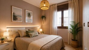Une chambre avec un grand lit, des lampes de chevet, un luminaire suspendu, une fenêtre avec des rideaux et deux tableaux accrochés au mur.