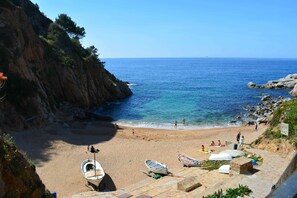 Une plage avec des bateaux, une falaise rocheuse et la mer.