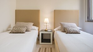 Et dobbeltværelse med to senge, hver med et hvidt sengetæppe og en pude med leopardprint. Et natbord med en lampe er placeret mellem sengene.