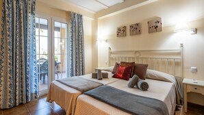 A hotel room with two beds, a balcony with curtains, a radiator, and wall-mounted artwork. - La Quinta de Isla Canela II - Isla Canela Golf GQHII2P2 (Isla Canela)