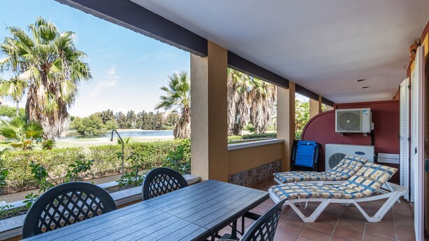 A covered outdoor area with a table and chairs, a lounge with cushions, and an air conditioning unit. - La Quinta de Isla Canela II - Isla Canela Golf GQHII2P2 (Isla Canela)
