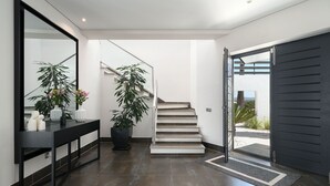 A modern interior with a staircase, a black-framed mirror, and a potted plant. - Villa Allegra - Quinta do Lago (Quinta do Lago)