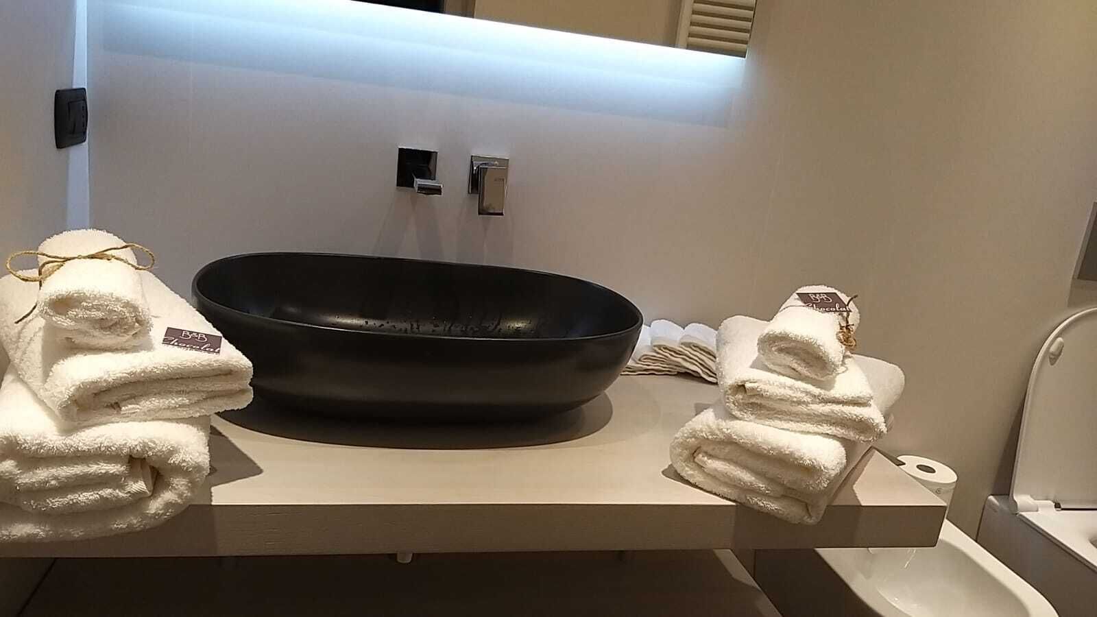 A bathroom with a black basin, white towels, and a white sink.