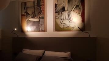 A hotel room with a bed, two paintings on the wall, and a nightstand.