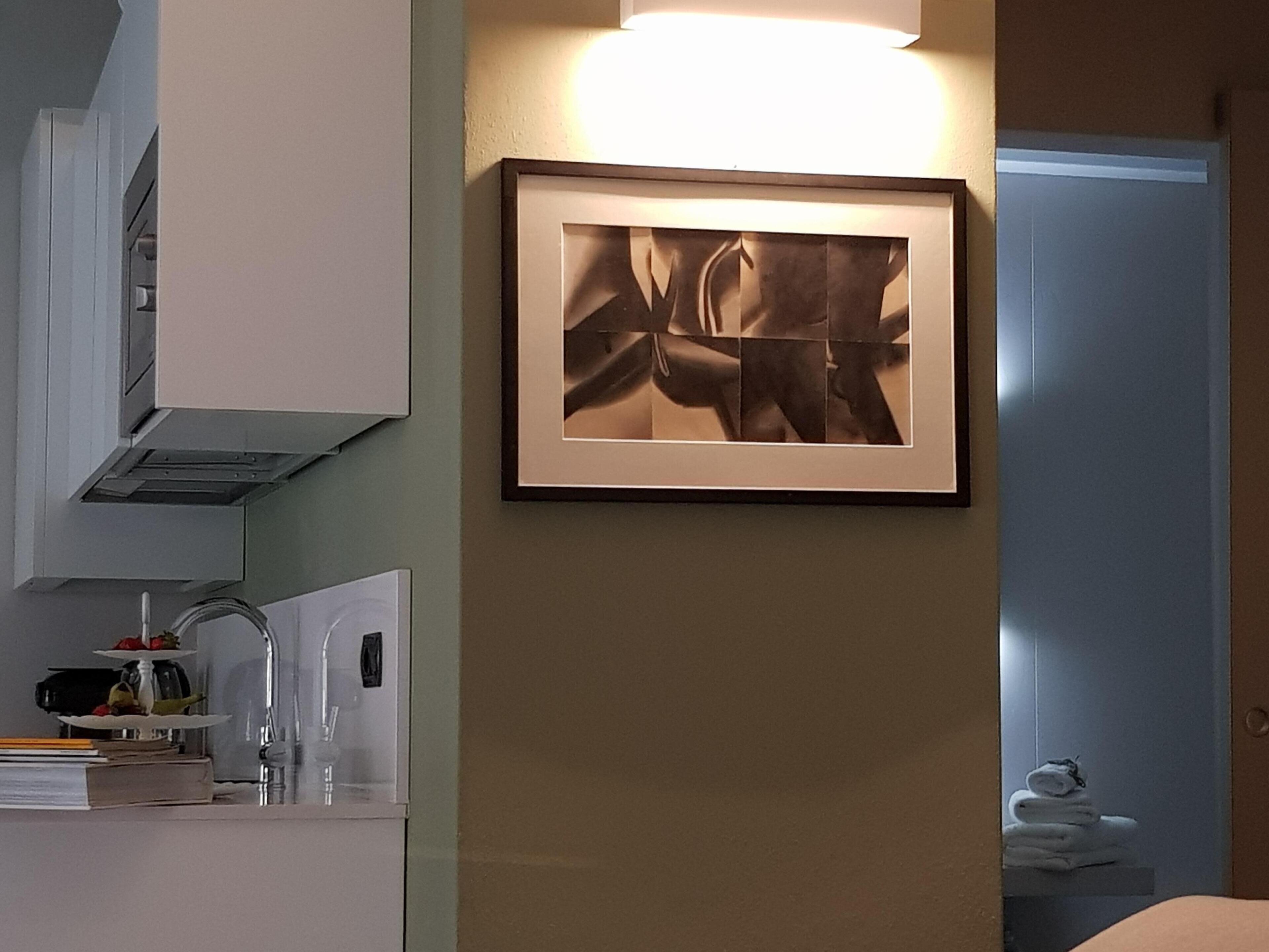 A framed abstract artwork on a wall, a kitchen area with a sink and a three-tiered stand, and a door with towels.