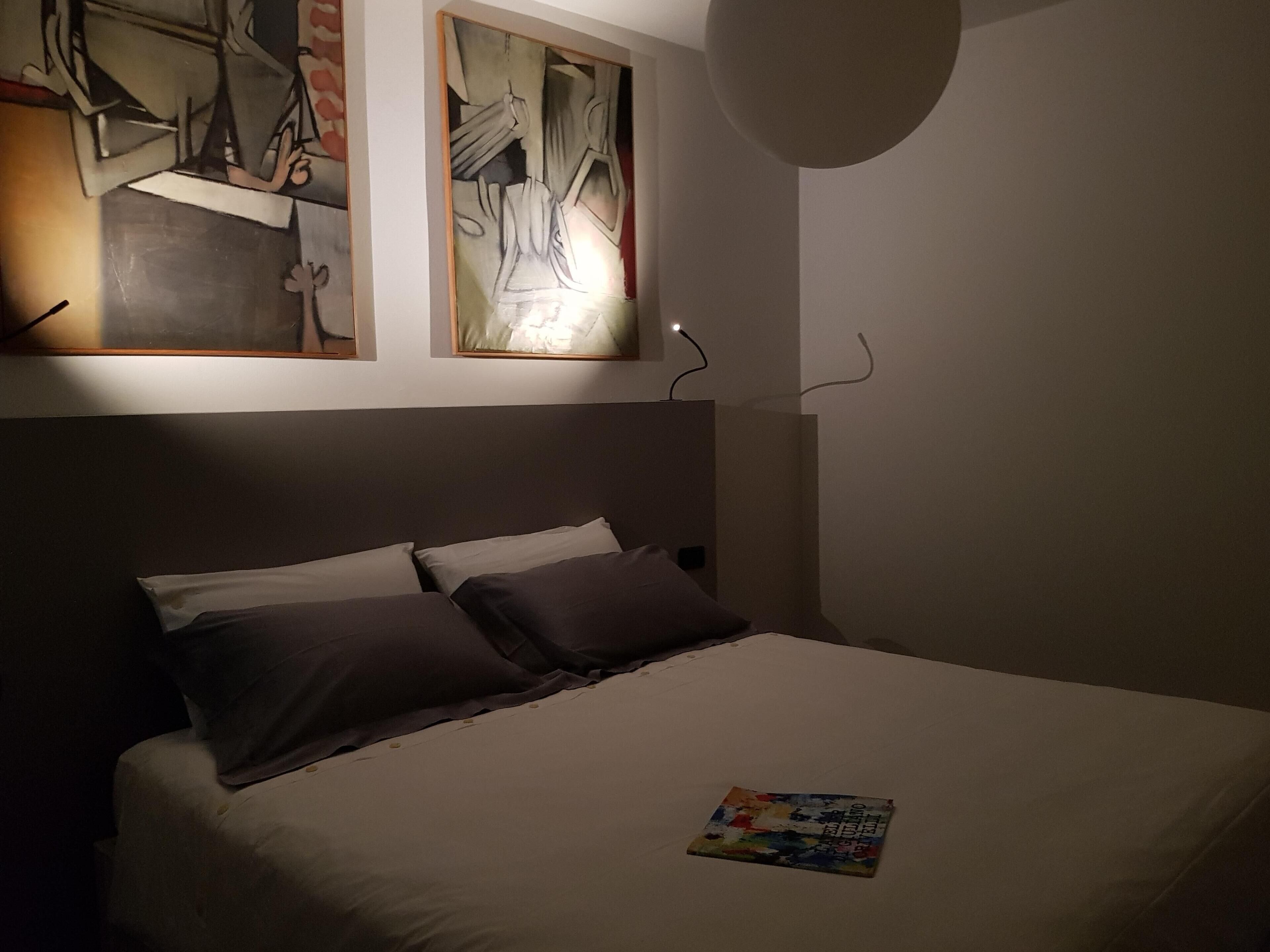 A neatly made bed with pillows, a wall-mounted artwork, and a small table with a magazine.