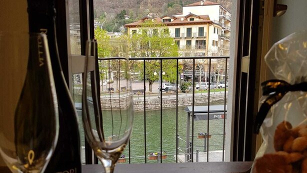 A balcony with a view of a hillside and buildings, a bottle of wine, two wine glasses, and a bag of snacks. - Chocolat la Mairie in Omegna (Omegna)