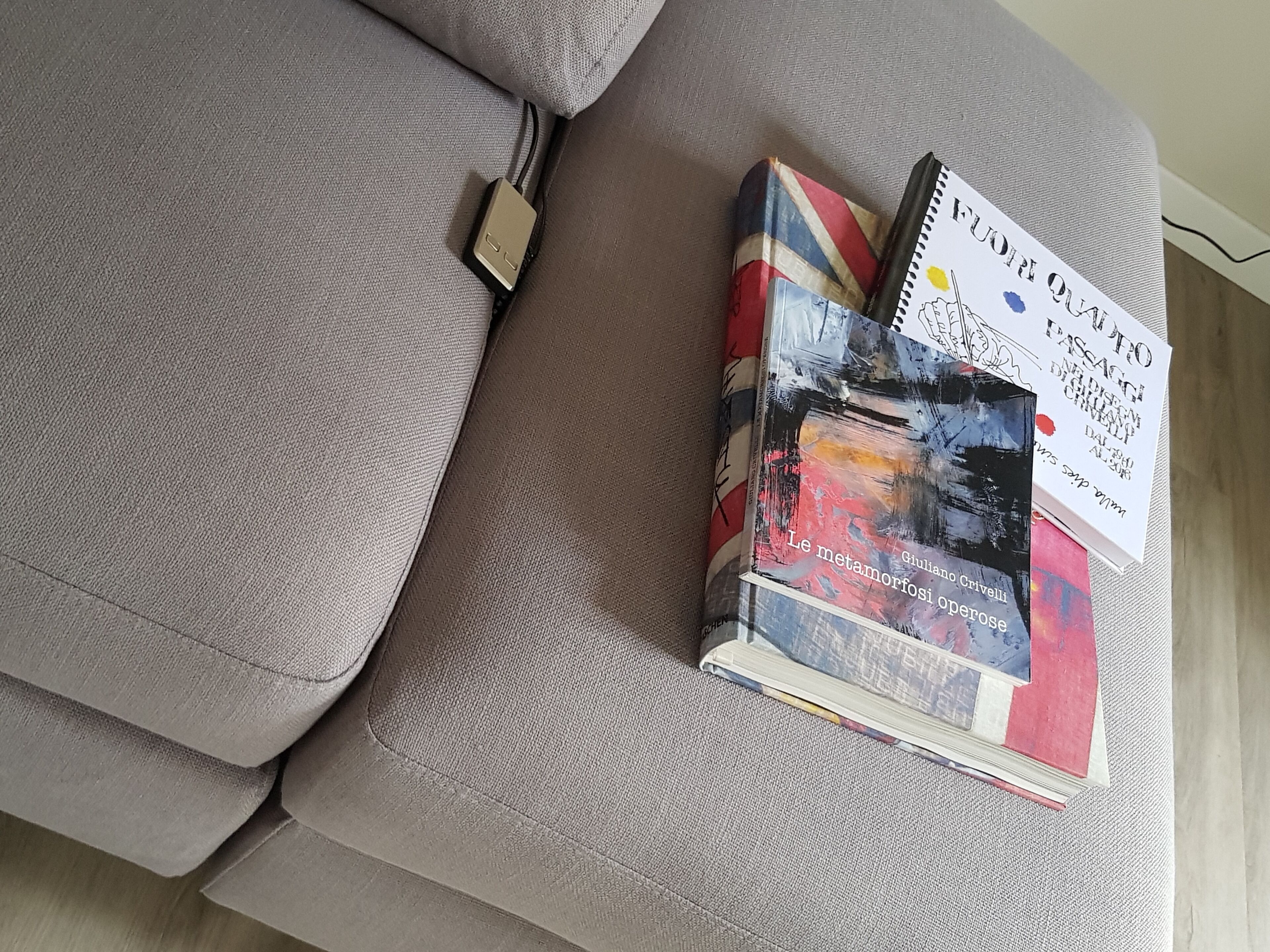 A grey sofa with a power strip and a stack of books.