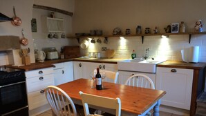Une cuisine avec des meubles blancs, une table en bois, deux chaises blanches et divers ustensiles et appareils de cuisine.