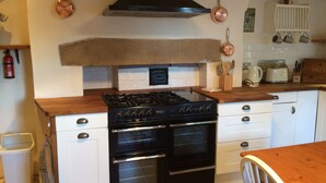 Une cuisine avec un poêle noir, deux fours, des armoires blanches et des casseroles en cuivre accrochées au mur.