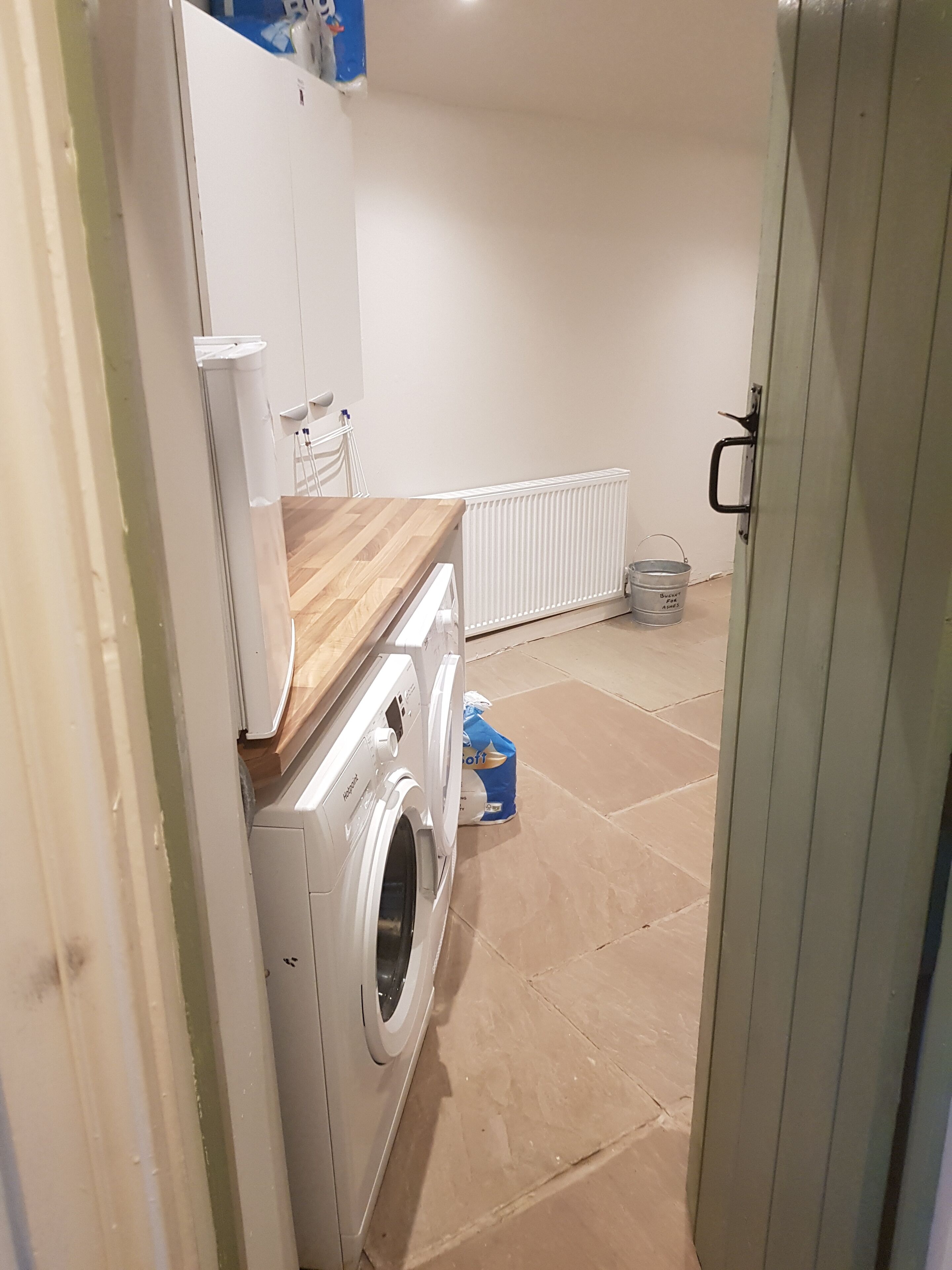 A laundry room with a washing machine, a radiator, and a bucket on the floor.