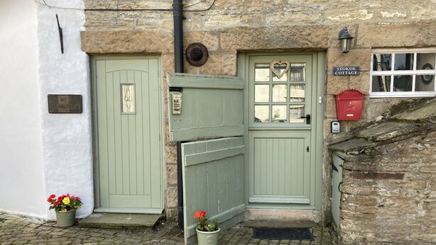 Une maison de campagne traditionnelle avec deux portes vertes, un mur en pierre et une boîte aux lettres rouge.