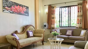 Ein Wohnzimmer mit einer Couch, einem Sessel, einem kleinen Tisch mit einer Vase und einem Ventilator.