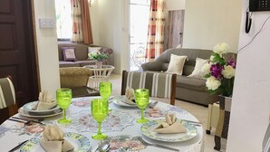 Un coin repas avec une table ronde dressée pour quatre personnes, agrémenté de verres verts et d’assiettes aux motifs bleus et jaunes.