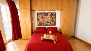 Une chambre d’hôtel avec un grand lit, une literie rouge, une armoire en bois et un plateau de petit-déjeuner posé sur le lit.