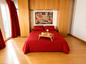 A hotel room with a large bed, red bedding, wooden wardrobe, and a breakfast tray on the bed. - Le Loft Boissy (Paris)